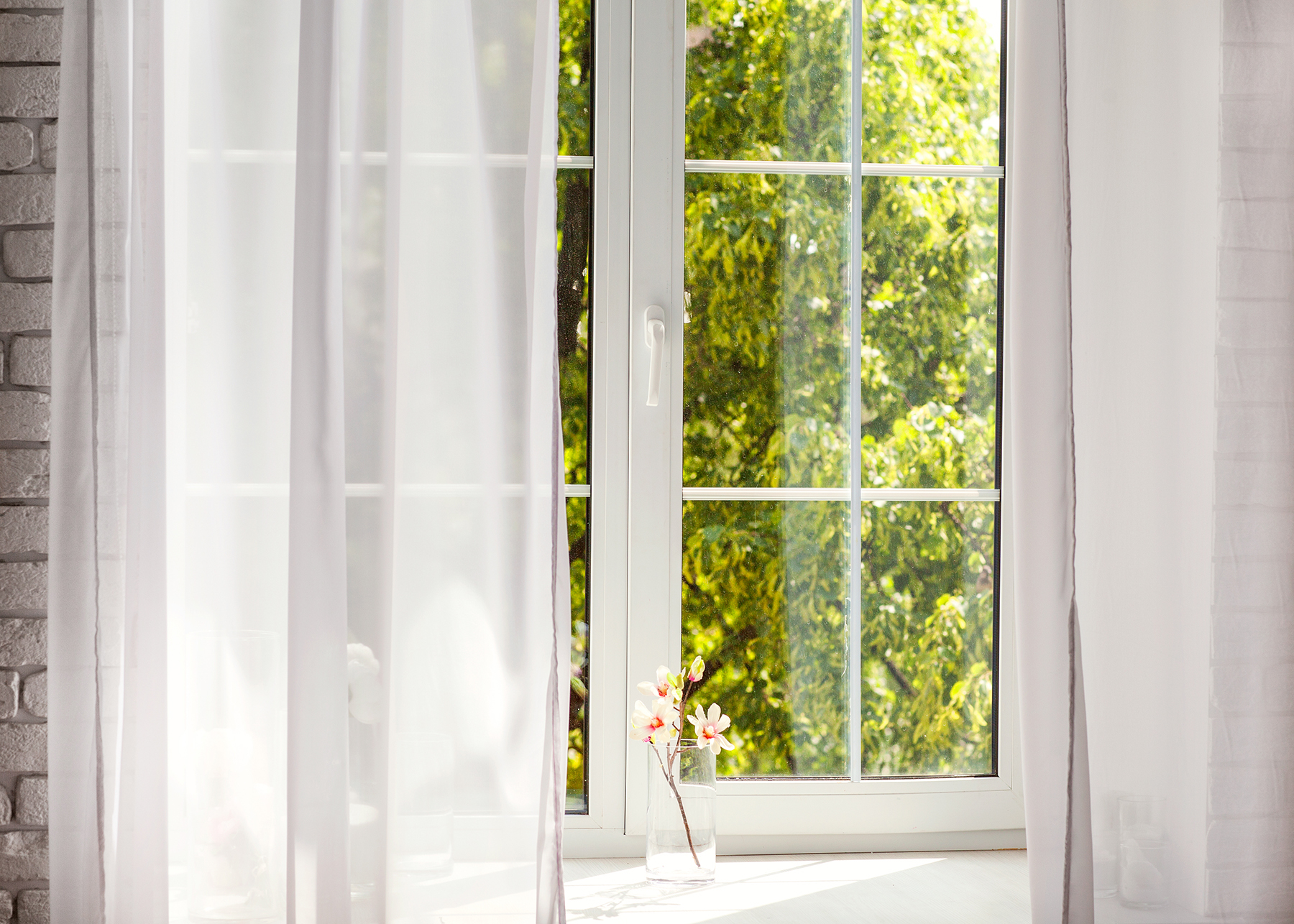 A window with white curtains and green trees outside. Natural light entering the room.