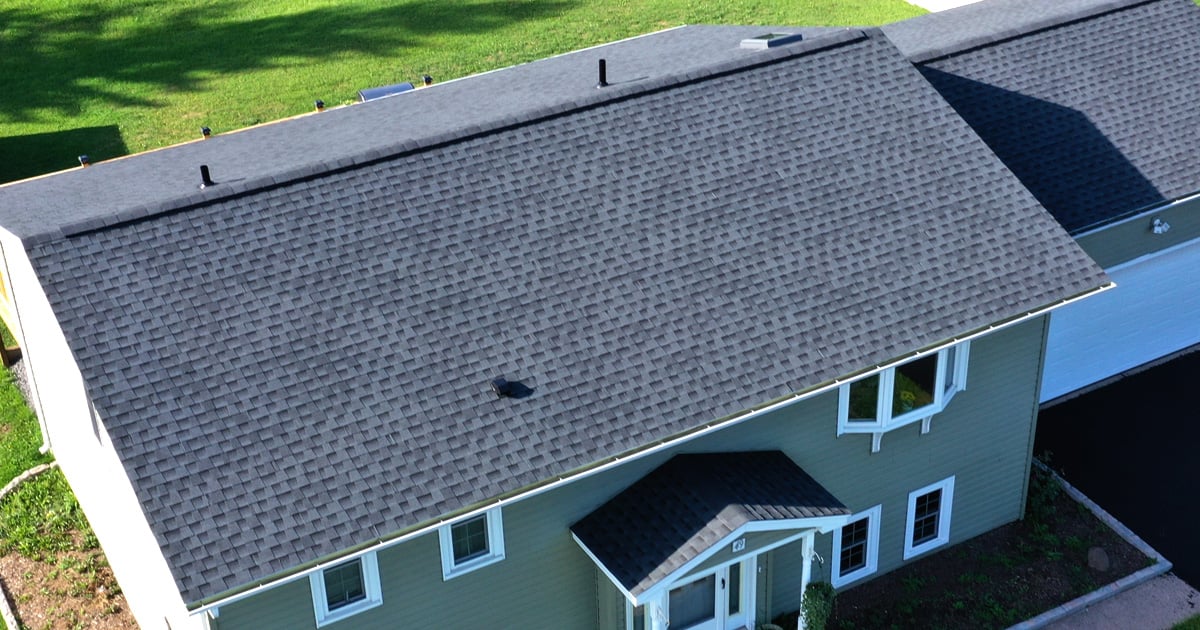 Aerial view of a house with dark gray roof and green walls. The house features white trim and a small front porch.