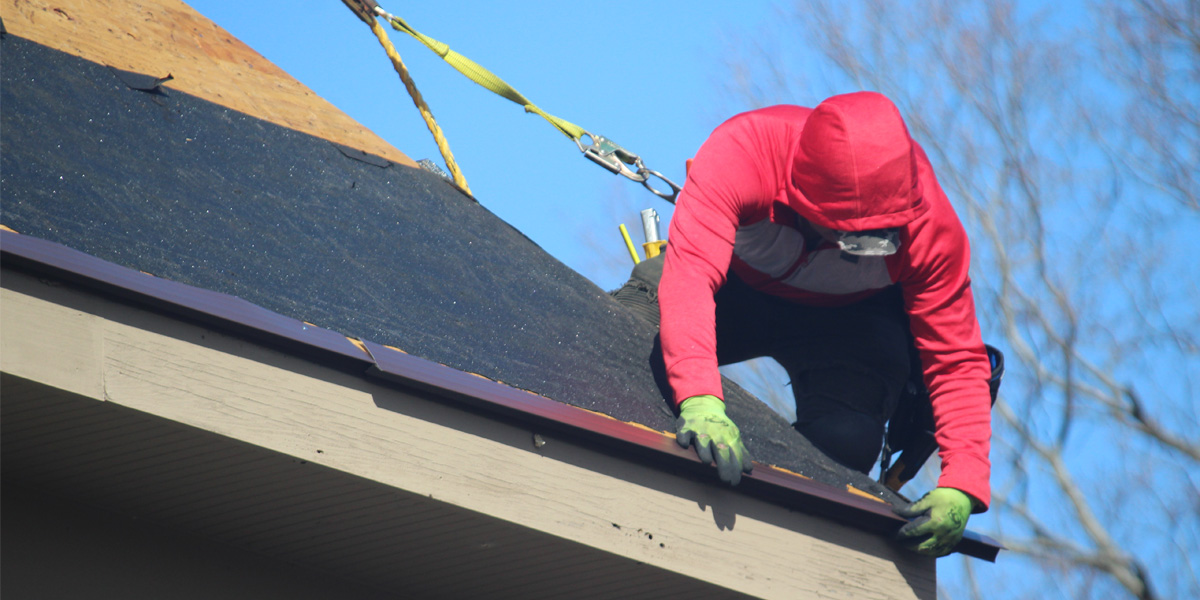Worker on roof installing shingles