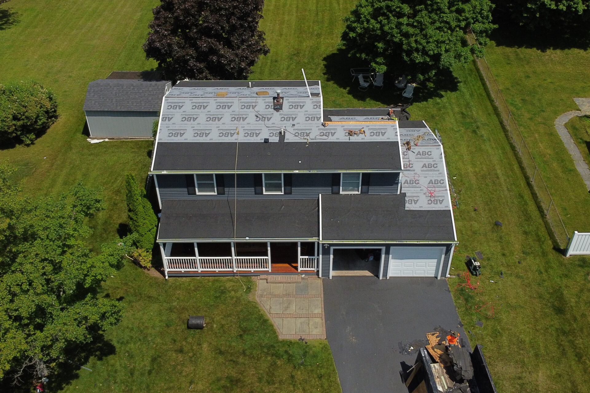 An aerial view of a house with partially installed new roofing materials. The house features a large front porch.
