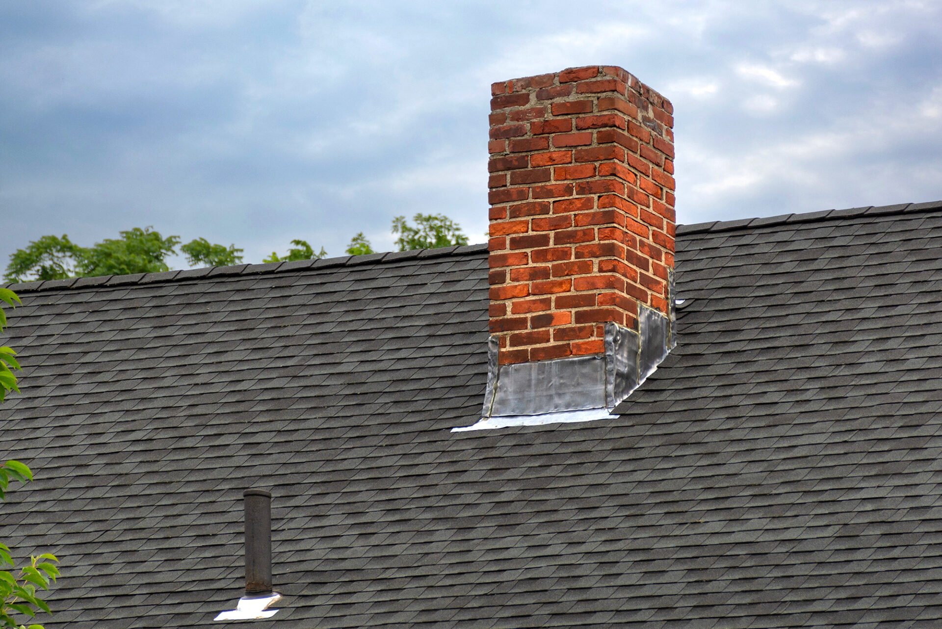 A roof with a brick chimney. The roof is covered in dark shingles.