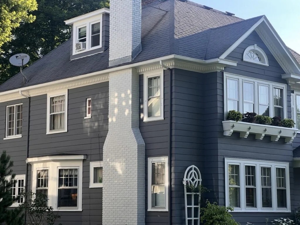 Gray house with white trim and balcony Large gray house with white trim and a balcony on the second floor. The house has multiple windows and a chimney.