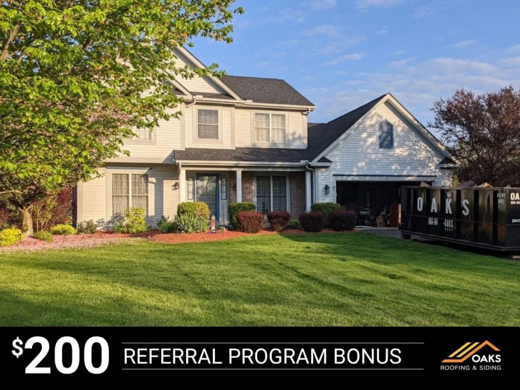 A large two-story house with a well-manicured lawn and a tree in the front yard. The house features a covered porch and a fenced-in area.