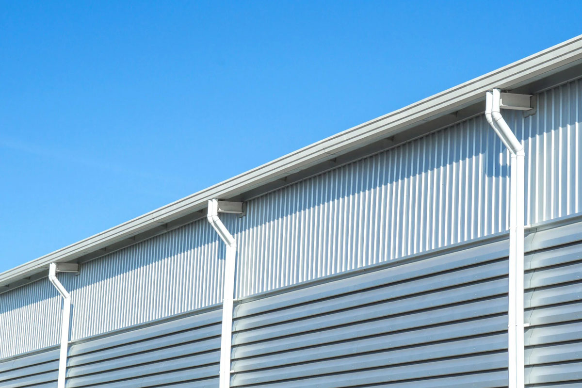 Close-up of building exterior with downspout Building exterior with white downspout and gutters. Corrugated metal wall