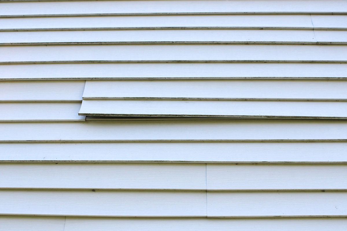 Damaged white vinyl siding on a building Damaged white vinyl siding. A broken piece of siding.