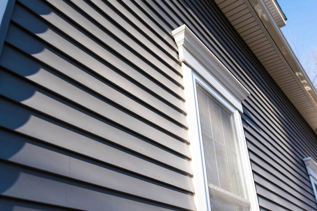 Gray house exterior with white window frame. Horizontal siding.