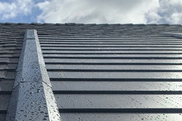 Gray roof shingles with a cloudy sky background. The shingles are wet.