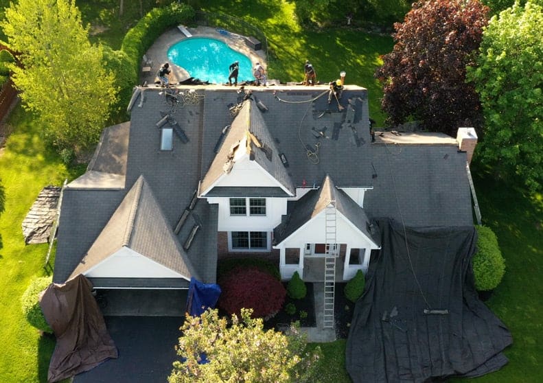 Aerial view of house with roof replacement A large house with a pool and trees. Roofing work in progress.