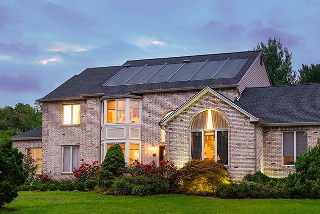 House with solar panels on the roof at sunset A large house with solar panels on its roof. The house is lit up from within.