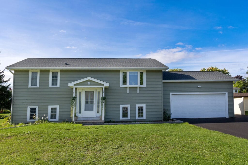 A two-story house with a gray exterior and white trim. The house features a large garage and a well-manicured lawn.