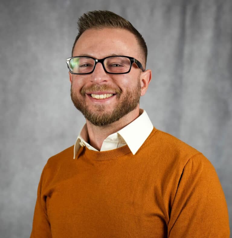 Smiling man in orange sweater and glasses portrait A man with a beard smiles wearing glasses and an orange sweater.