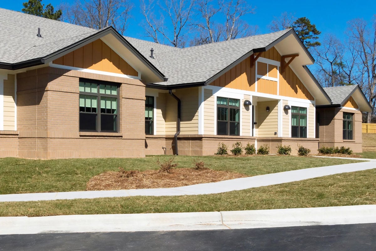 Modern house with gable roof and sidewalk A single-story house with a gray roof and beige walls. The house has a covered porch.