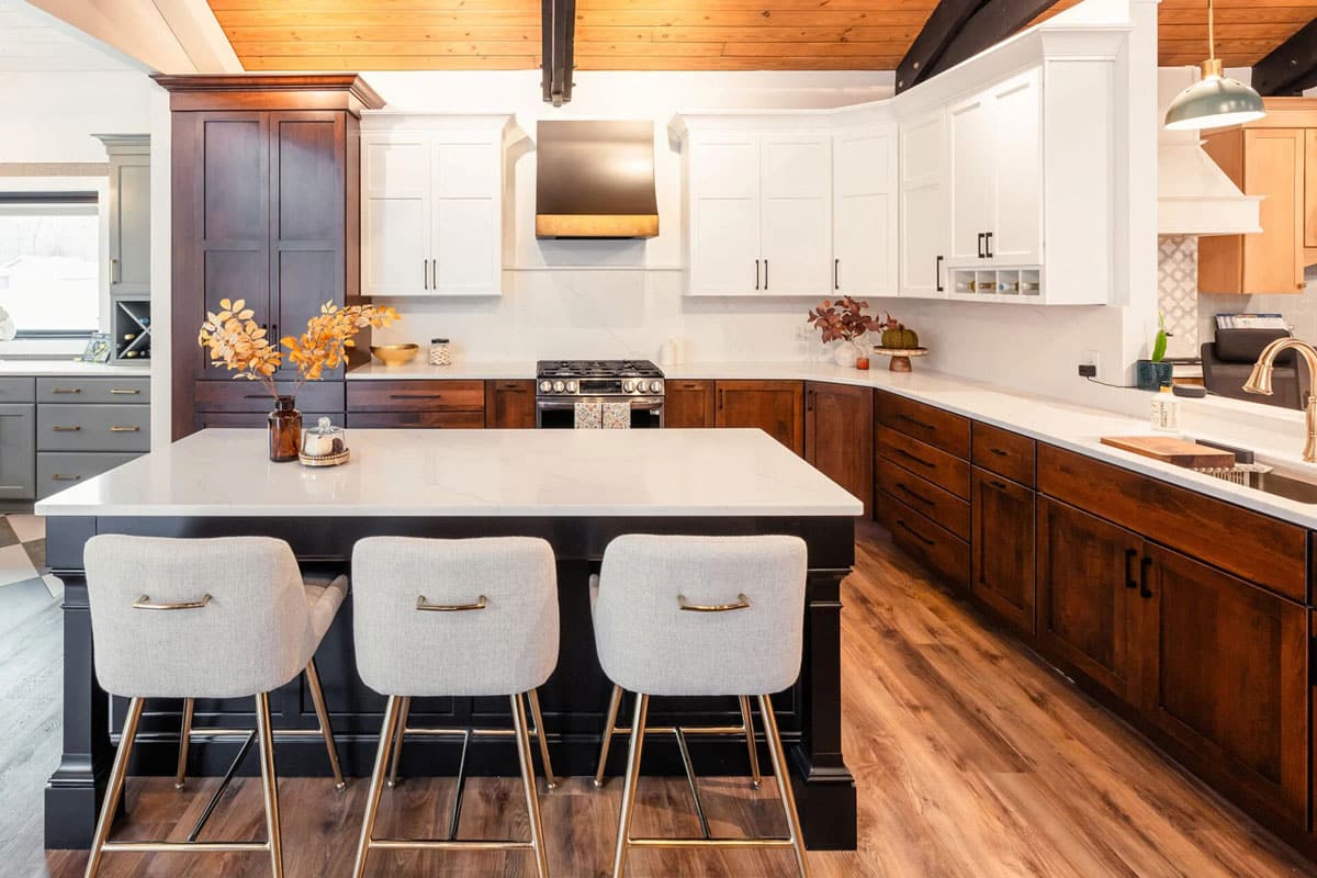 A modern kitchen with a large island and white chairs. The kitchen features dark wood cabinets and white countertops.