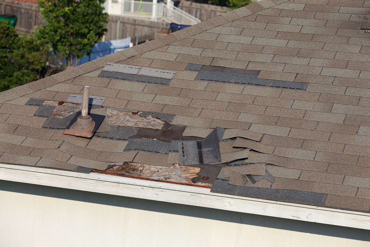 Damaged Roof Shingles A roof with damaged and missing shingles. Roof repair is needed.