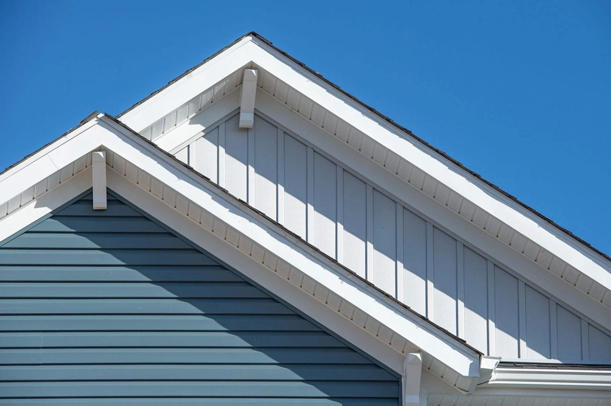 Roof of house with blue siding and white trim A house roof with blue siding and white trim under a clear blue sky. The roof has a gable design with white eaves.