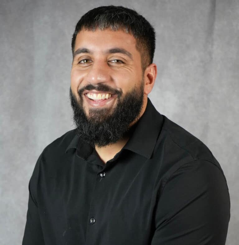 Smiling man with beard in black shirt A man with a beard smiling at the camera. He is wearing a black shirt.