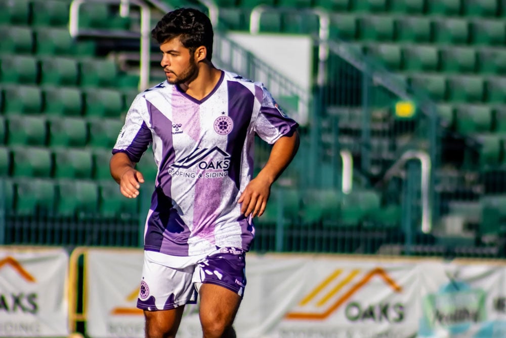 A young man playing soccer. He is wearing a purple and white jersey.