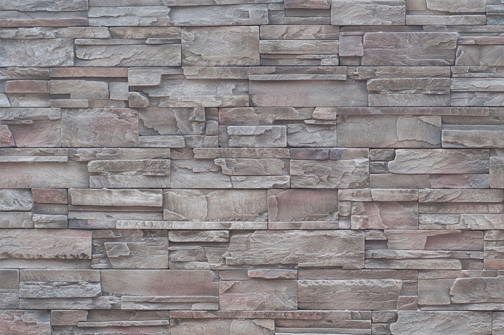 A stone wall with a mix of gray and brown colors. The stones are arranged in a staggered pattern.