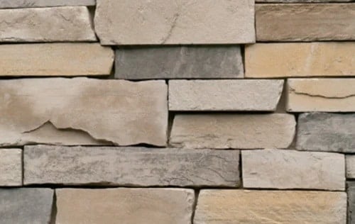 Stacked stone wall with beige and gray bricks A stone wall with a mix of beige and gray bricks. The stones are stacked horizontally.