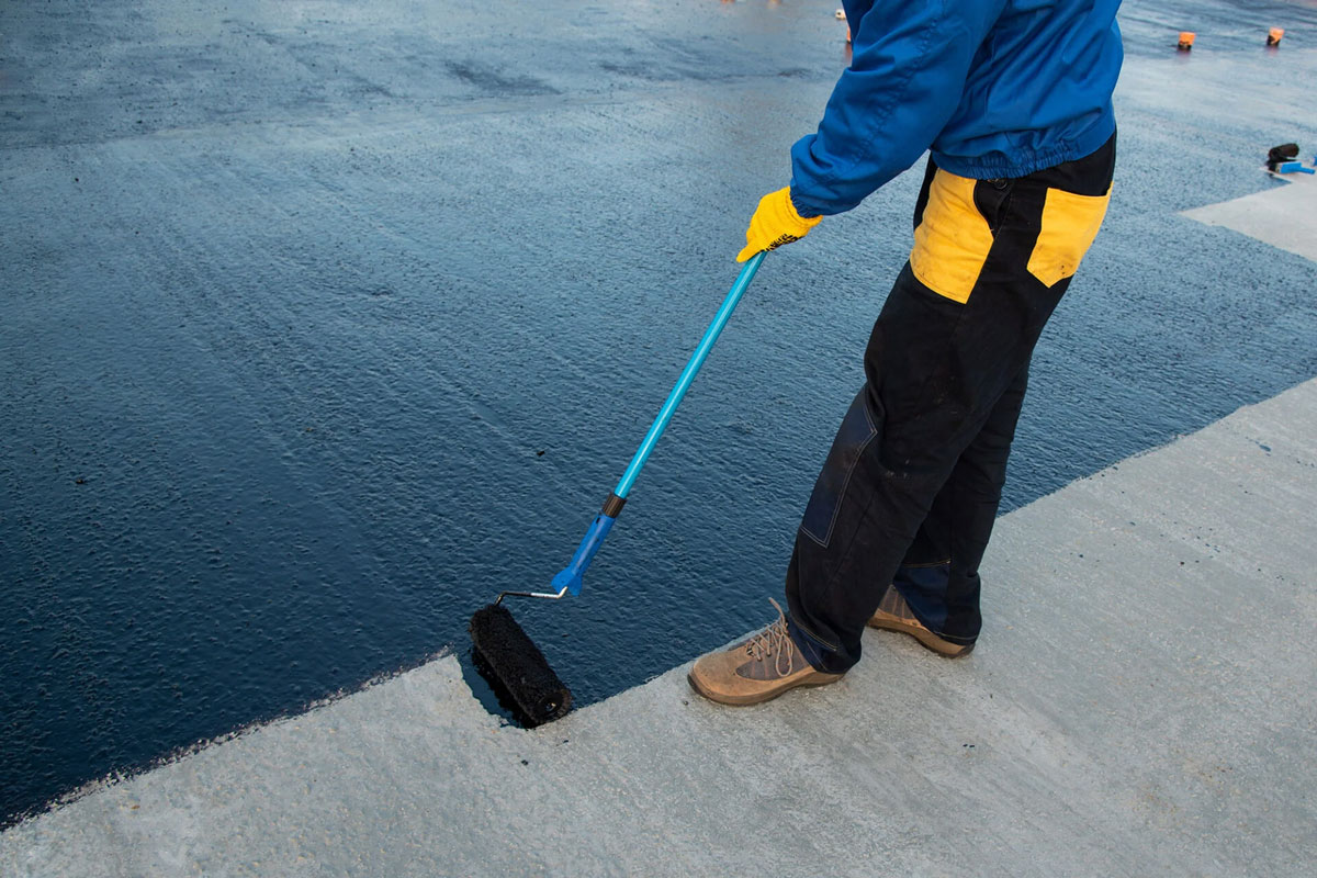 Worker applying sealant to concrete surface Man in protective gear applying sealant.