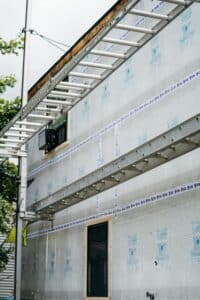 Building under construction with exterior insulation and scaffolding. A doorway and window are visible.