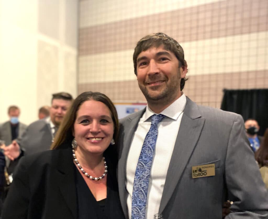 A man and woman in business attire smiling at a networking event. They appear to be colleagues or industry professionals.