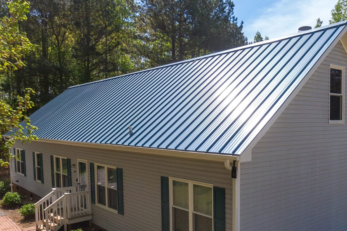 A house with a metal roof surrounded by trees. The house has a small porch and green shutters.
