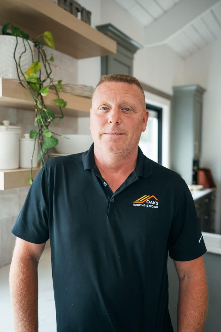 man in black polo shirt with company logo A man wearing a black polo shirt with a company logo on the left side of his chest. He appears to be standing in a modern kitchen or office.