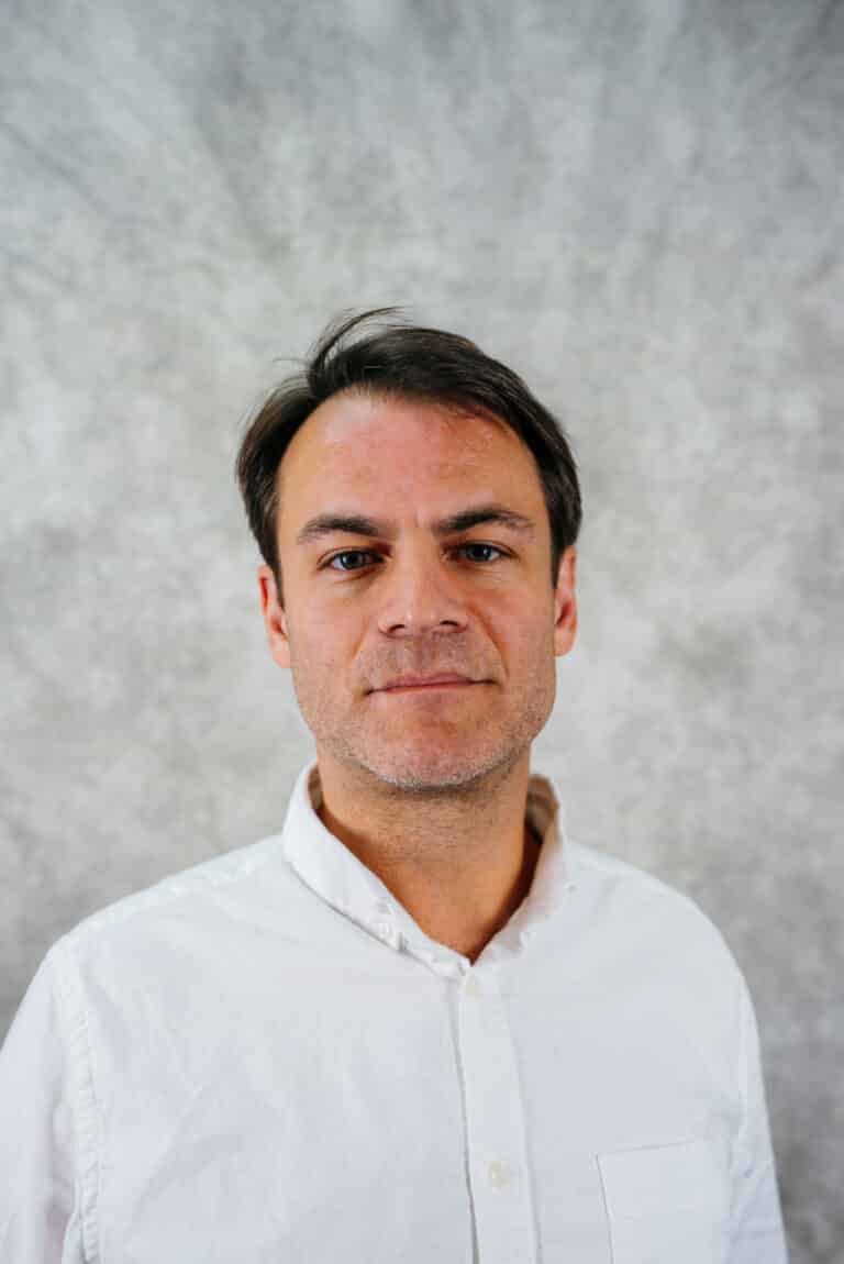 Man in white shirt looking at camera A man with dark hair and a white shirt. He is looking at the camera.