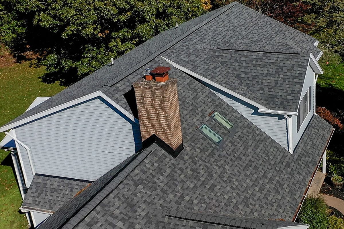 A high-angle view of a residential roofing system with a chimney and skylight, showing architectural details. The image depicts a modern home's roofing structure.