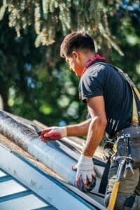 Man in work gloves cleaning a gutter. Worker on roof.