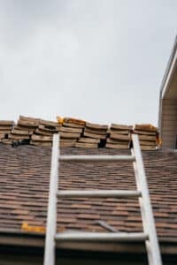Roof repair in progress. A ladder leans against a roof with missing shingles.