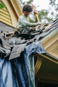 A worker repairing a roof on a house. The worker is focused on fixing the roof.