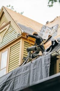 A roofer in a harness working on a roof. The roofer is installing a new roof.