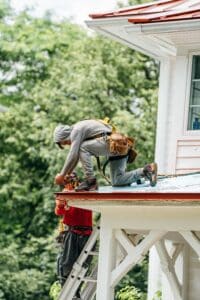 A man in a tool belt works on a roof. He is installing roofing material.
