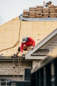 A roofer in a red jacket working on a roof. The worker is installing new roofing materials.
