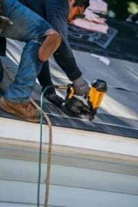 A roofer using a nail gun on a roof.