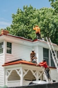 Three roofers working on a house with orange roofing materials. They are ensuring a safe and proper installation.