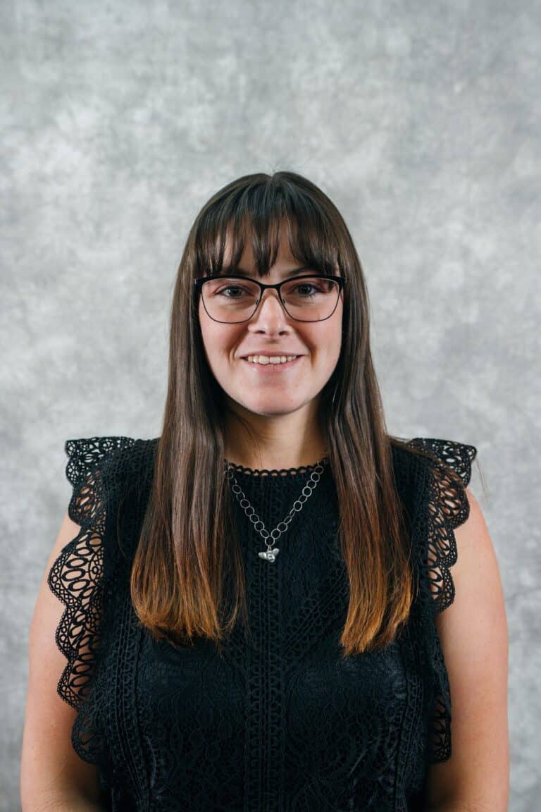 Woman with glasses and long brown hair smiles Portrait of a woman with glasses and brown hair. She is wearing a black top.
