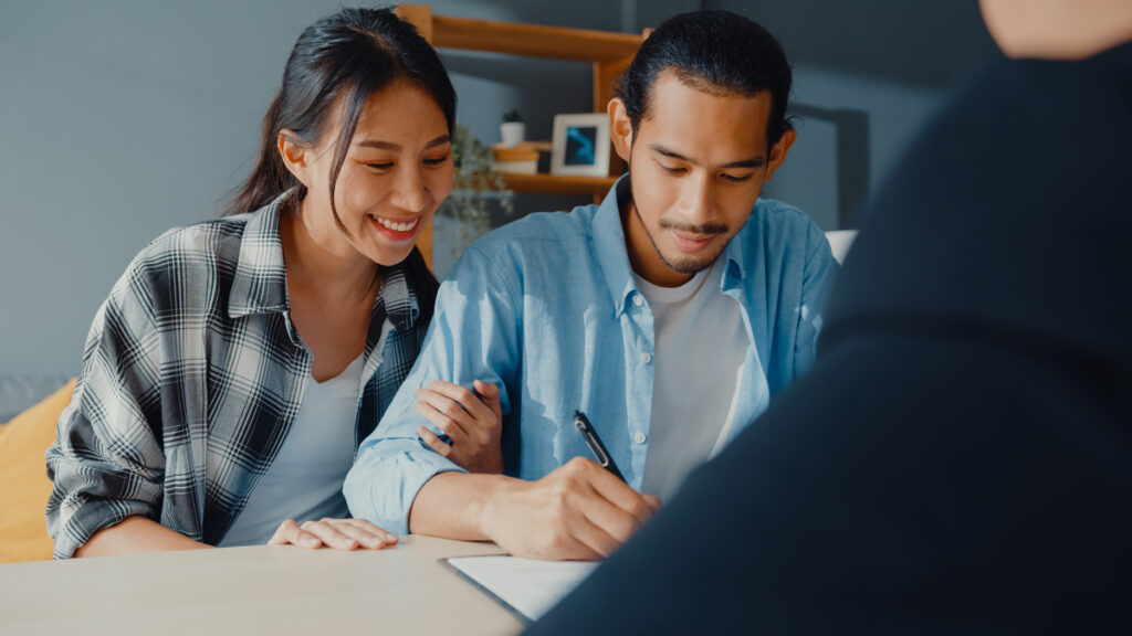 A couple signing documents with an agent. They appear to be in a discussion.