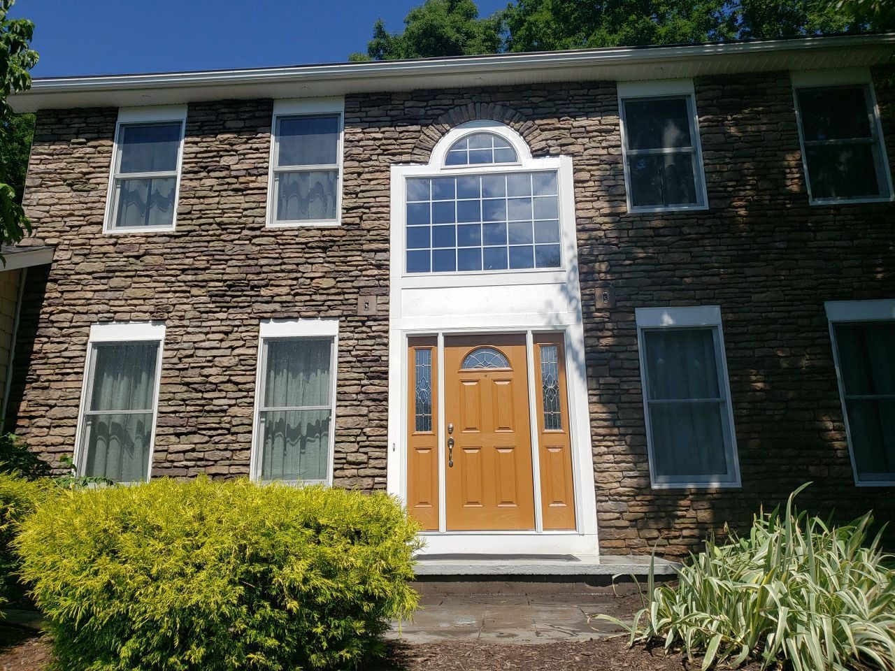A brown brick house with white trim and a wooden front door. The house has multiple windows and a well-manicured lawn.