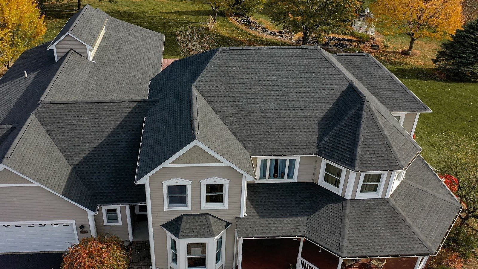 Aerial view of a large house with a gray roof and white trim. The house has multiple windows and a well-manicured lawn.