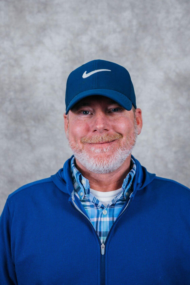 An older man with a white beard wearing a blue Nike cap and a blue sweater.