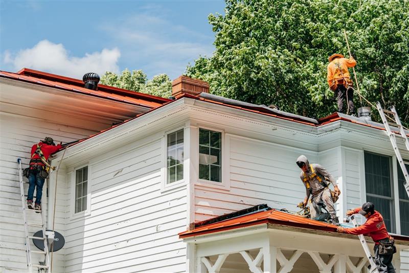 Workers installing new roof on a white house. Roofers on ladders and roof.