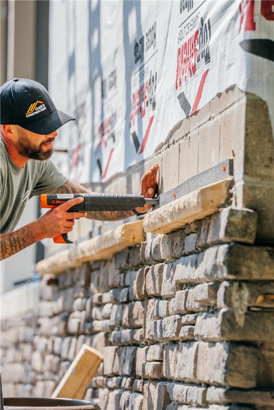 Man in a baseball cap laying stone wall. Construction worker using a level and trowel.
