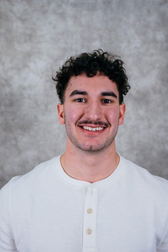 a young man smiling at the camera. He has curly hair.