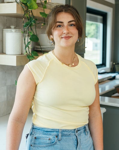 A young woman smiling at the camera. She is standing in a kitchen.