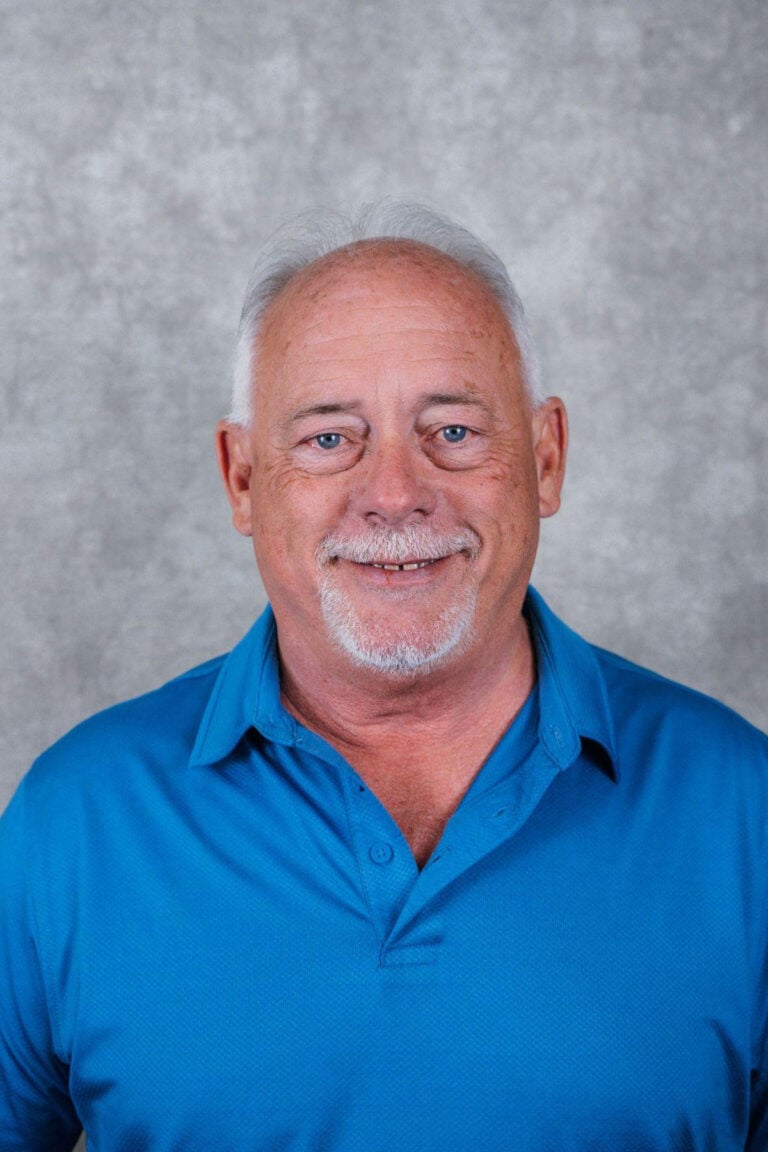 Portrait of an older man smiling. He is wearing a blue polo shirt.