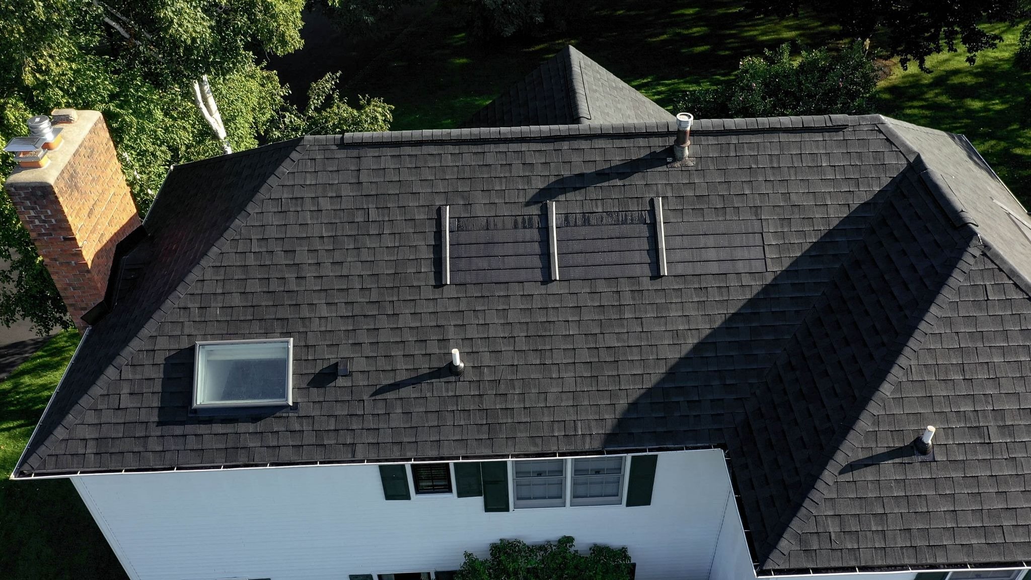 A house with a dark gray roof and white walls. The roof features several skylights and chimneys.
