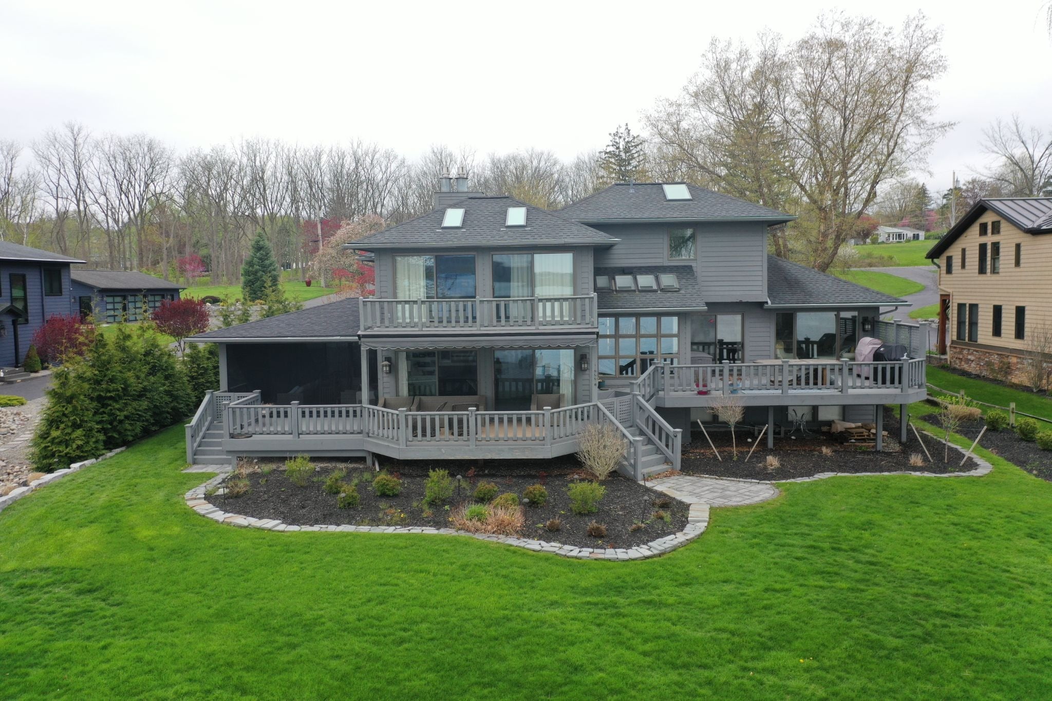 A large gray house with a spacious green lawn and a deck